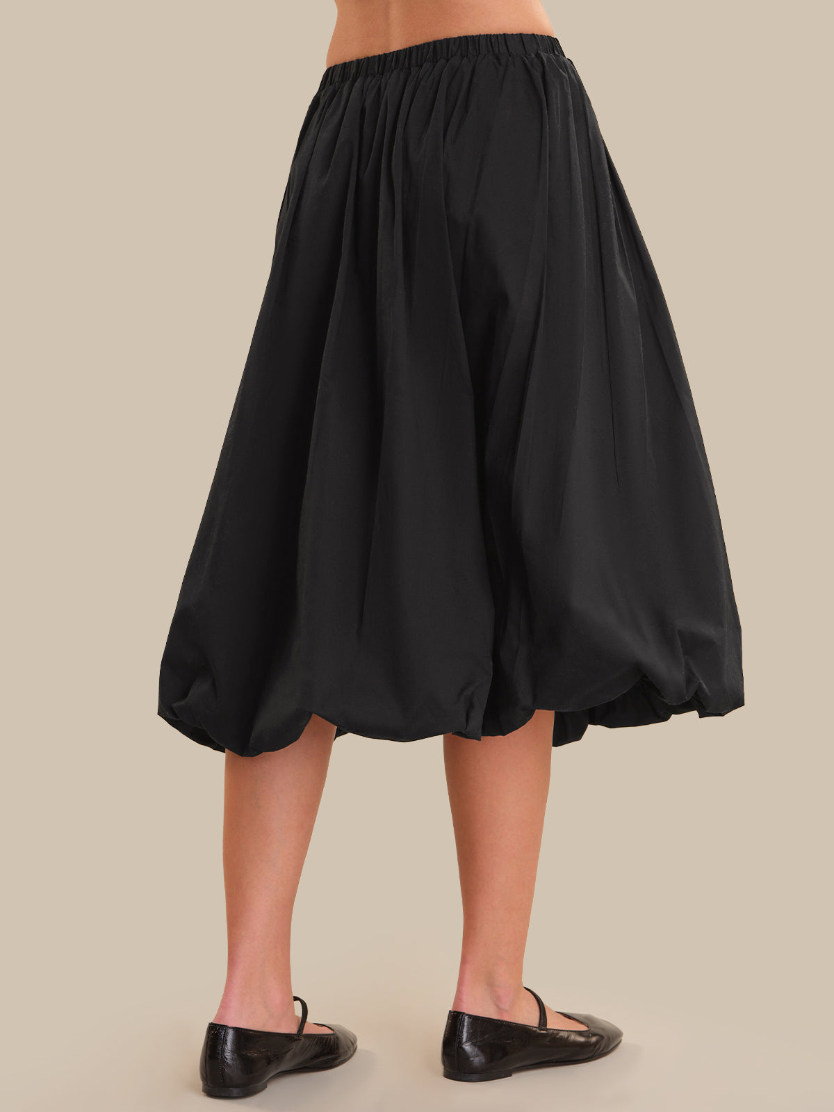 Black skirt worn by a person on a beige background