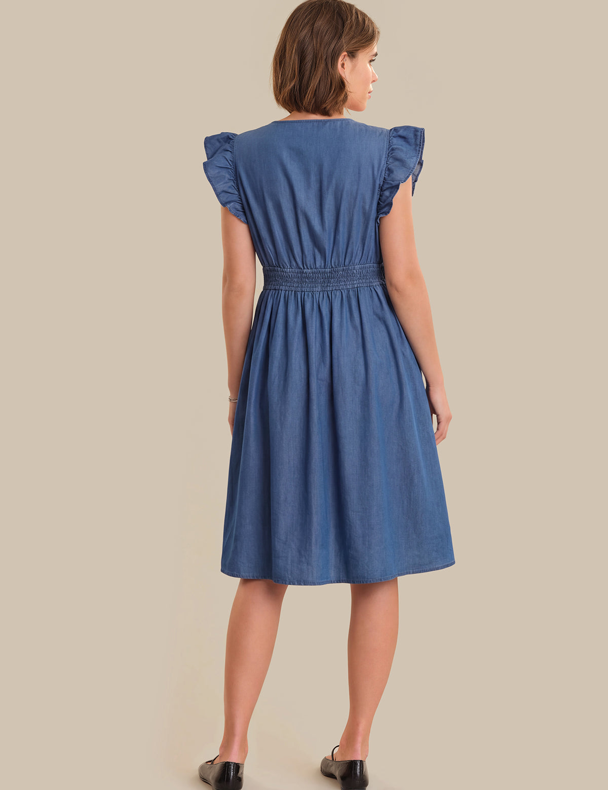 Woman wearing a blue dress with ruffled sleeves on a beige background