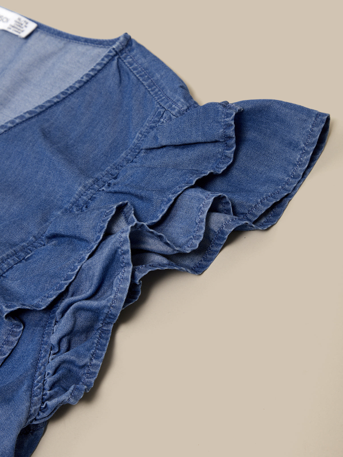 Blue denim shorts with ruffled details on a beige background