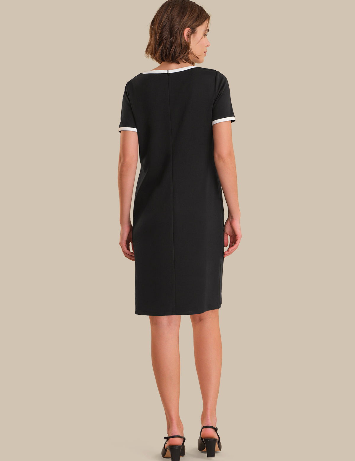 Woman wearing a black dress with white trim on a beige background