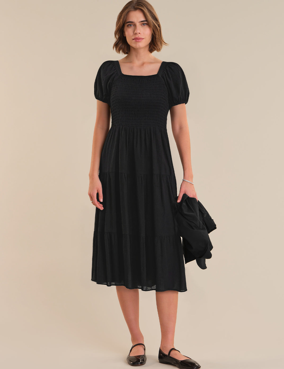 Woman wearing a black dress with puff sleeves against a beige background