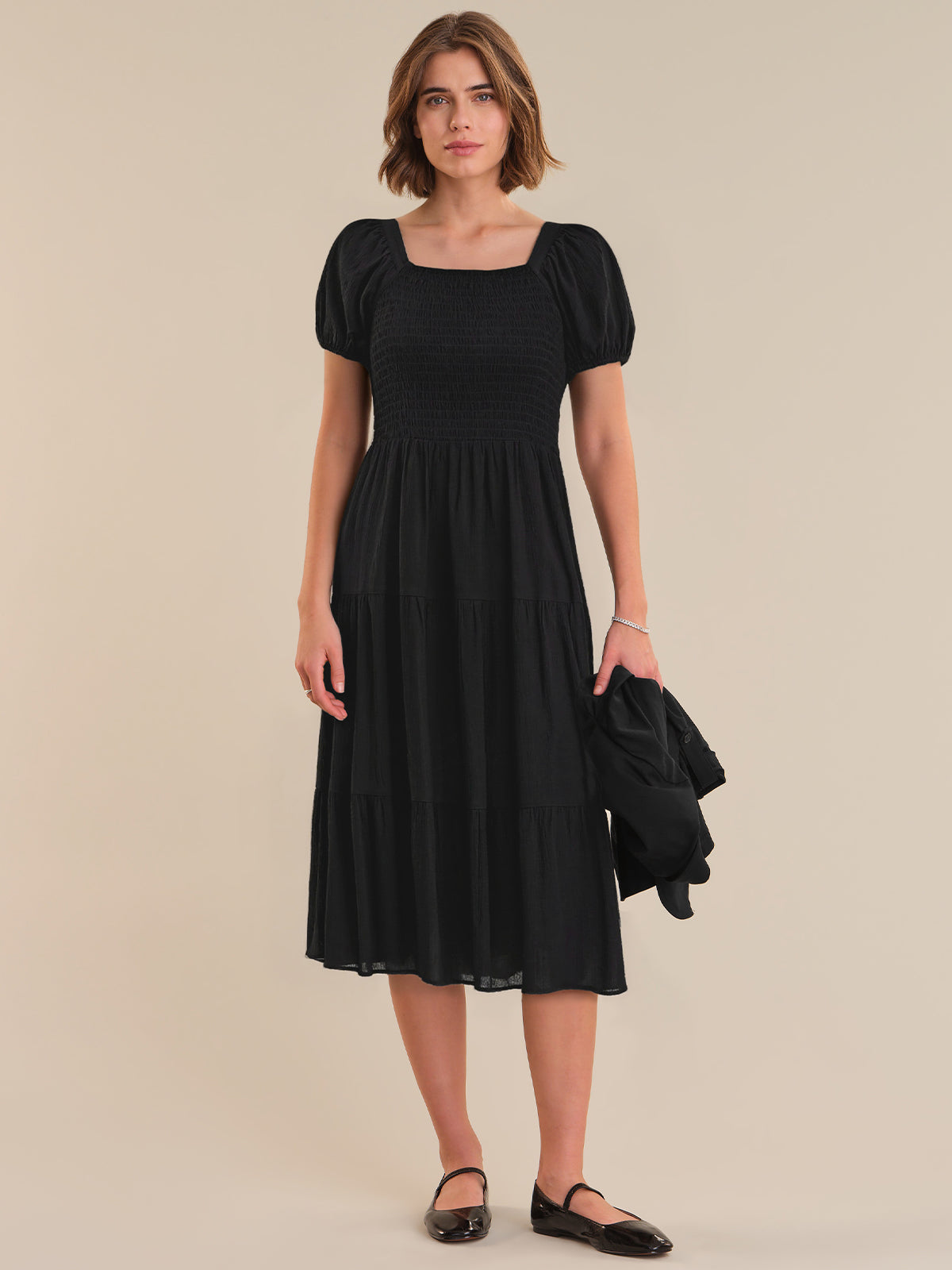 Woman wearing a black dress with puff sleeves against a beige background