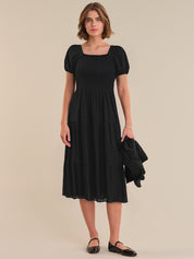 Woman wearing a black dress with puff sleeves against a beige background