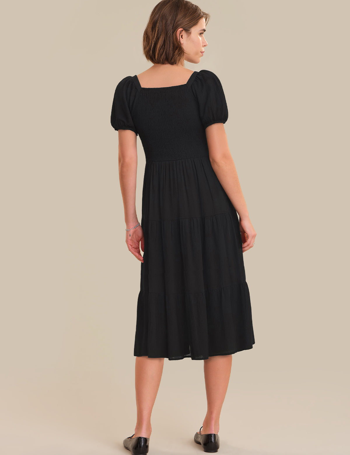 Woman wearing a black dress with puff sleeves on a beige background