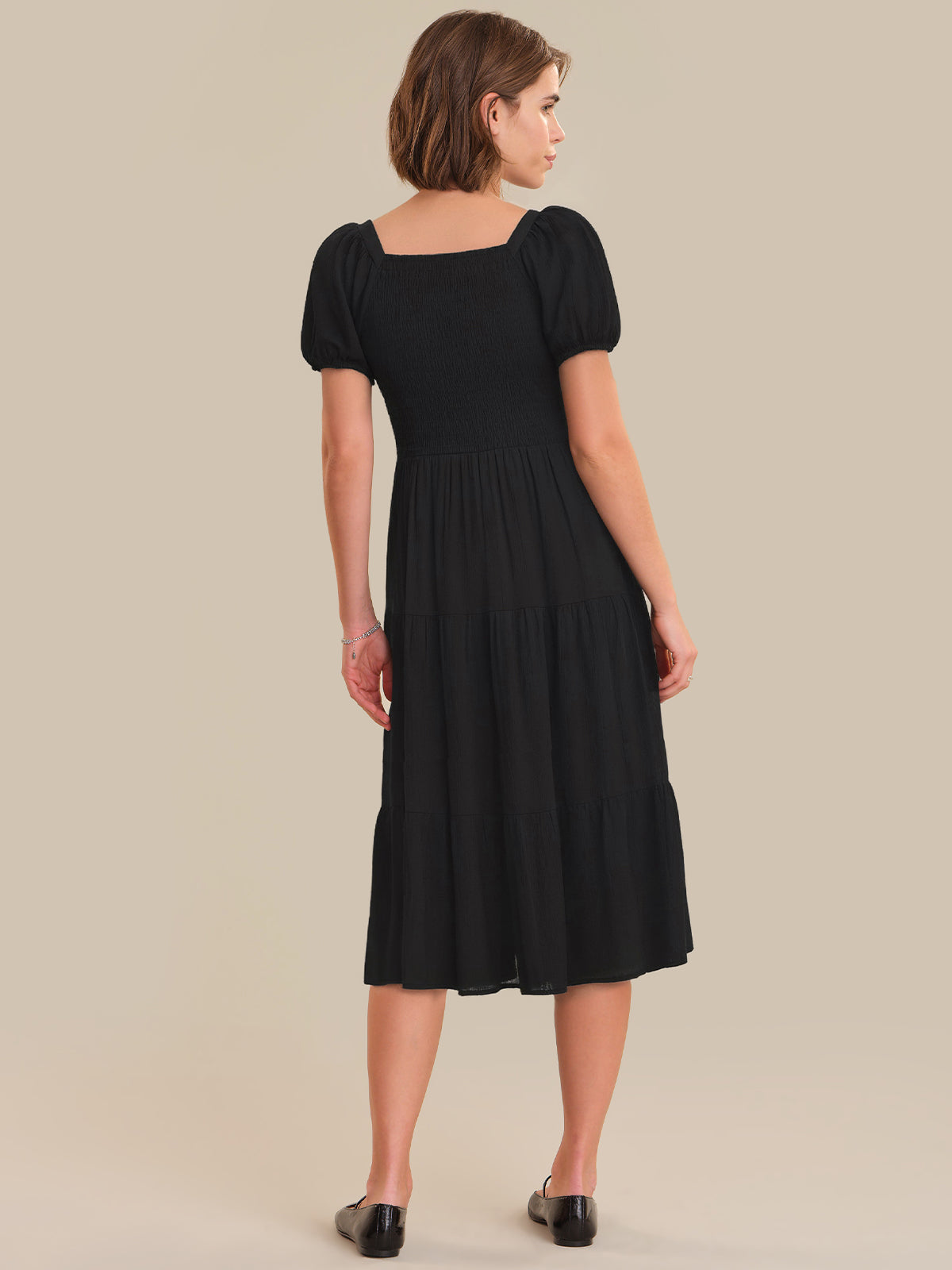 Woman wearing a black dress with puff sleeves on a beige background