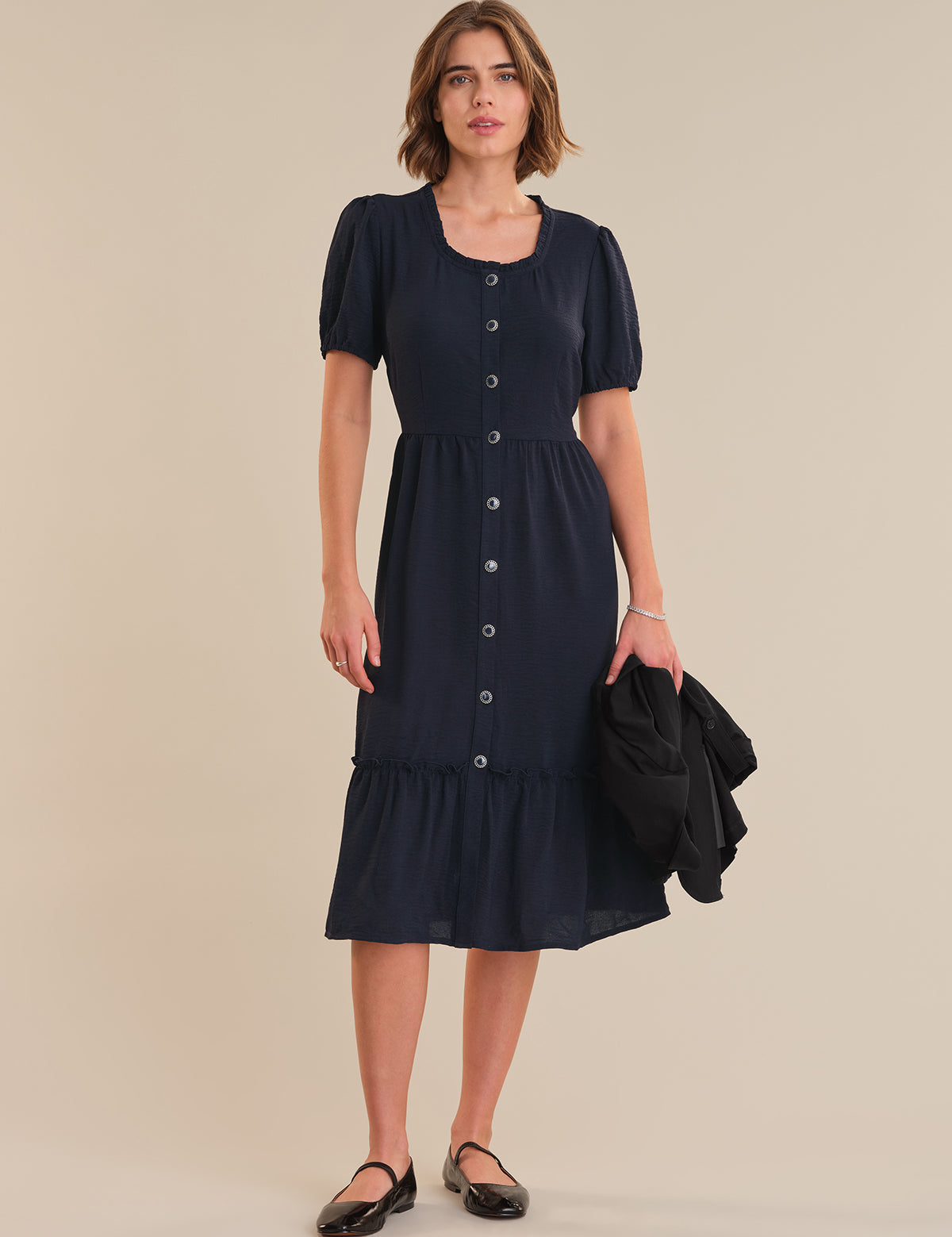 Woman wearing a navy dress with puff sleeves against a beige background