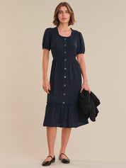 Woman wearing a navy dress with puff sleeves against a beige background