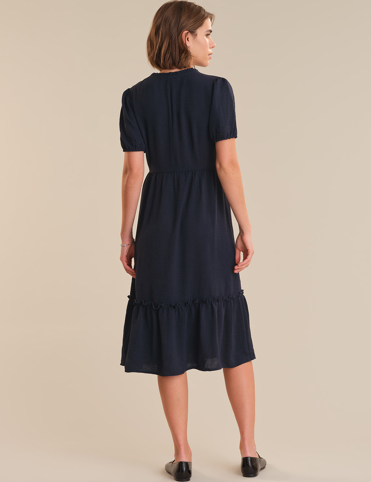 Woman wearing a navy blue dress with a ruffled skirt on a beige background