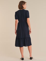 Woman wearing a navy blue dress with a ruffled skirt on a beige background