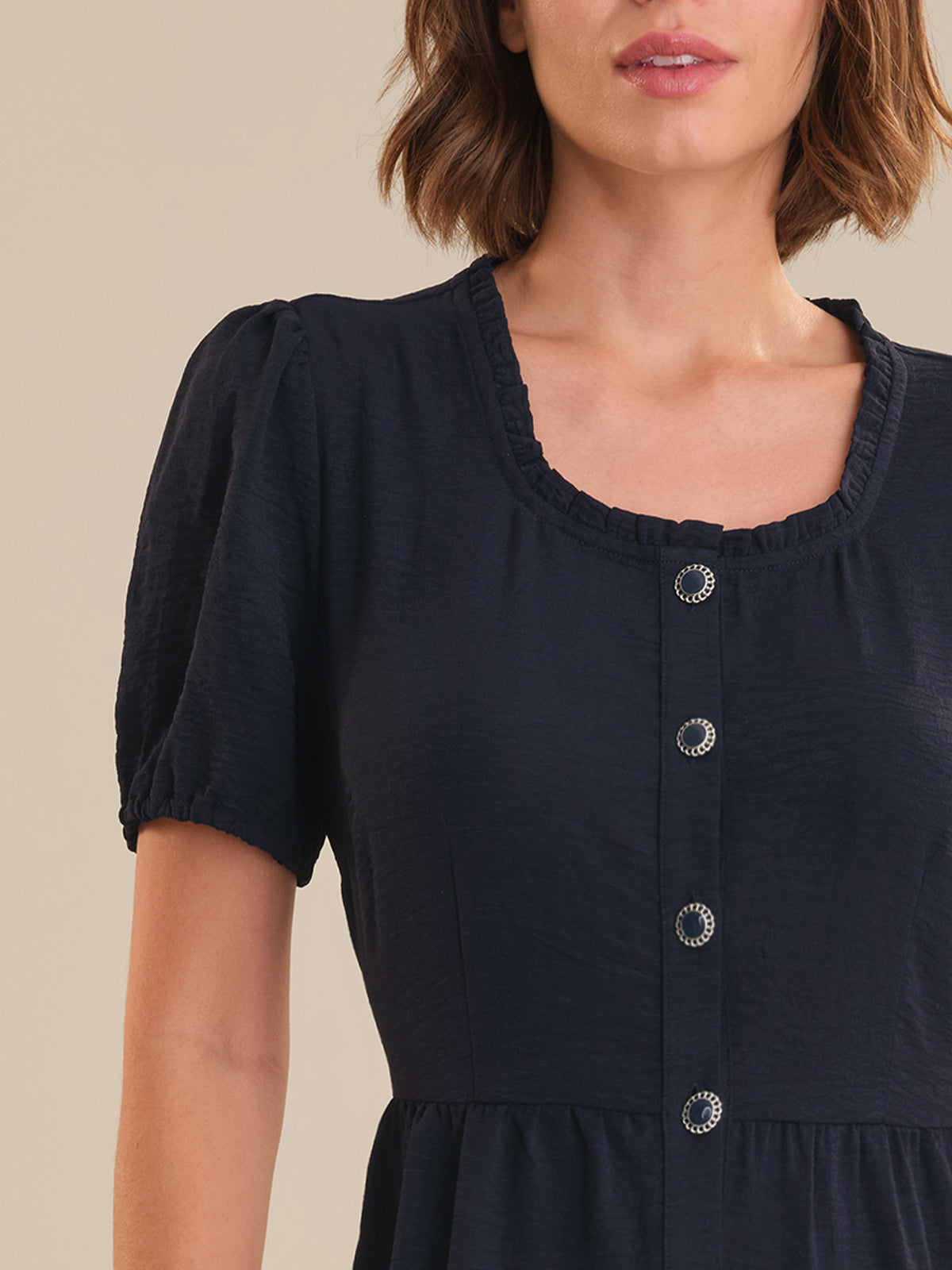 Navy blue dress with short sleeves and button details on a beige background