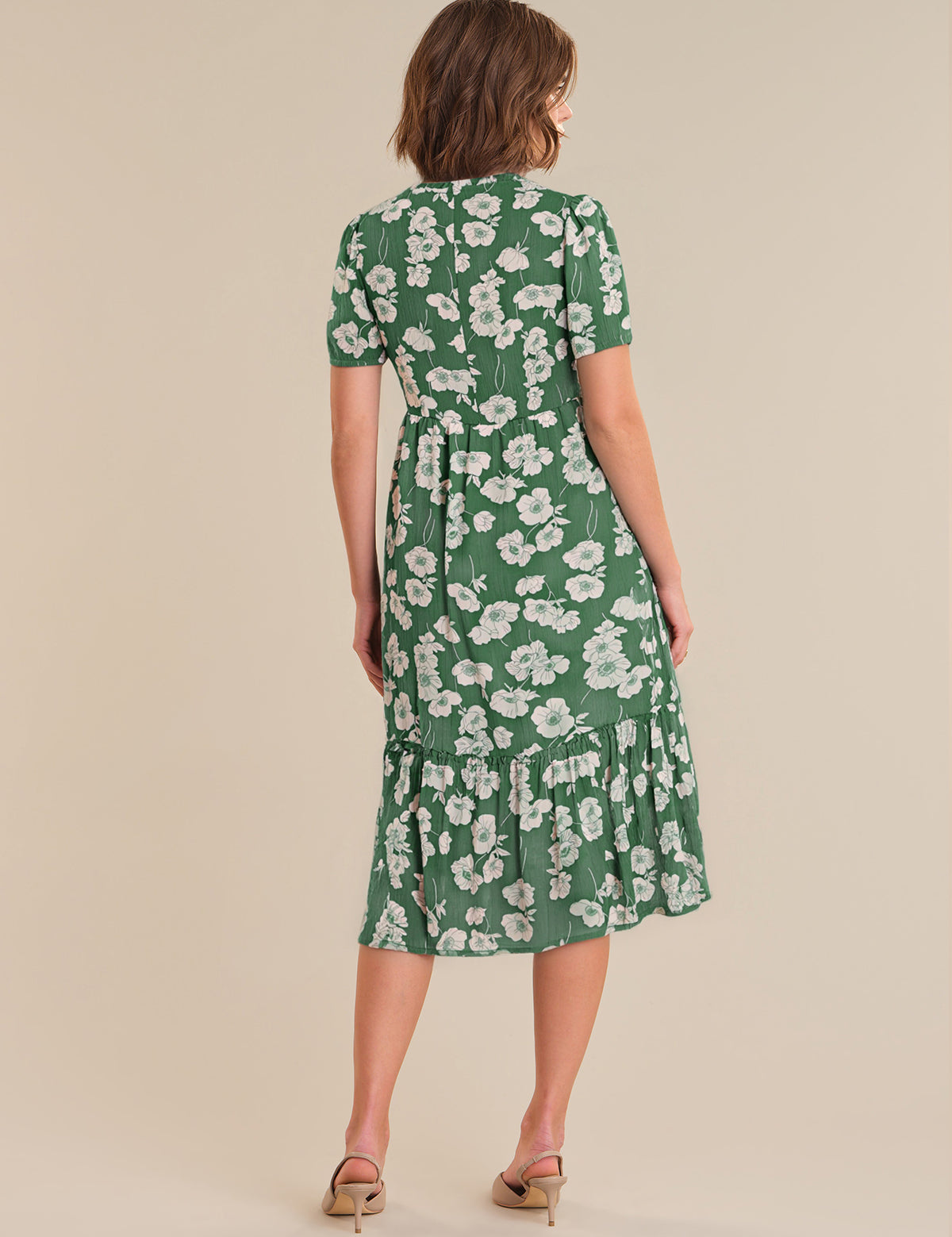 Woman wearing a green floral dress against a beige background