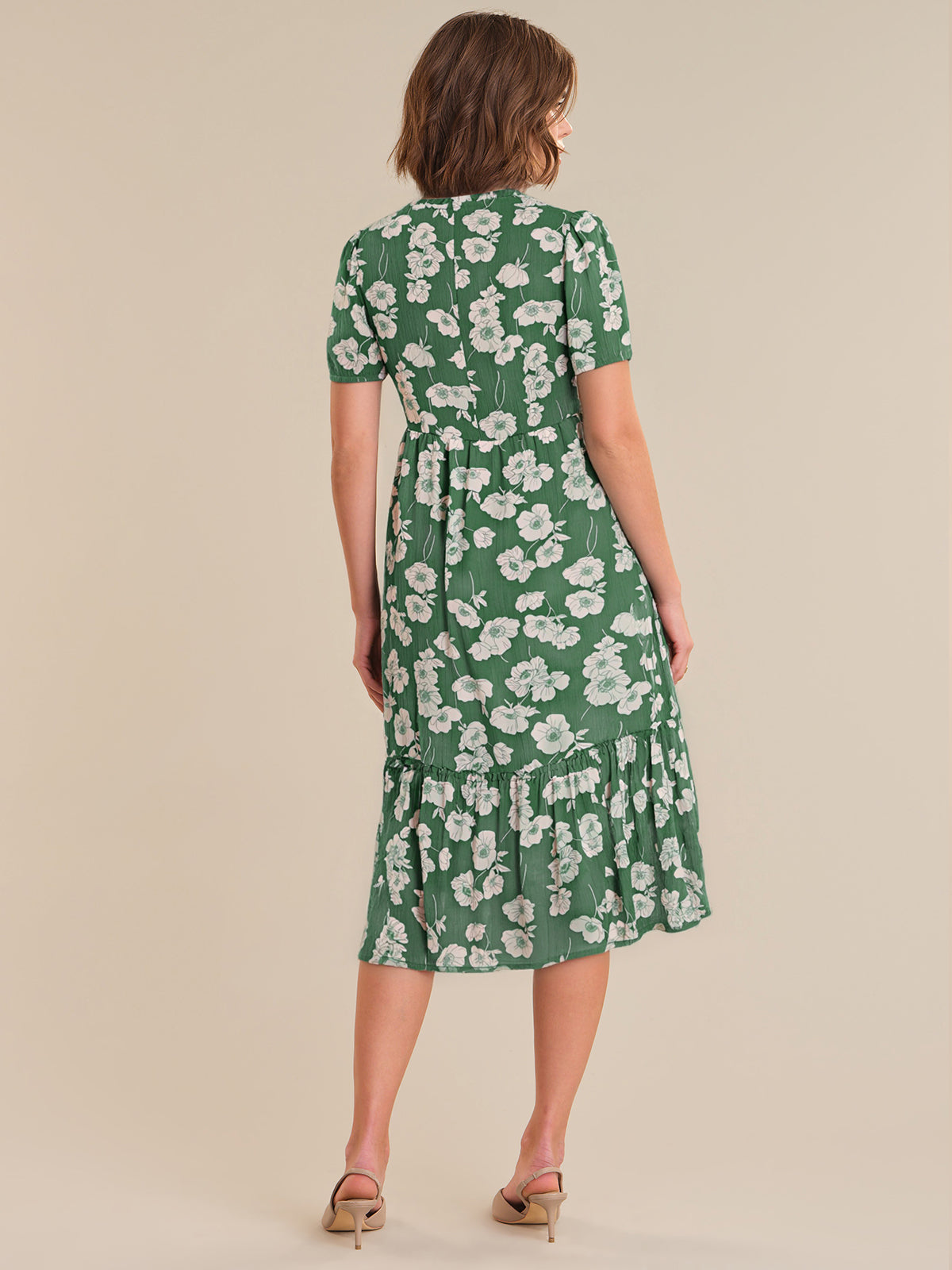 Woman wearing a green floral dress against a beige background