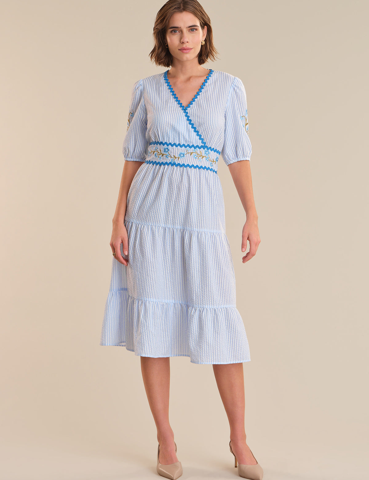 Woman wearing a blue and white striped dress with a belt on a beige background