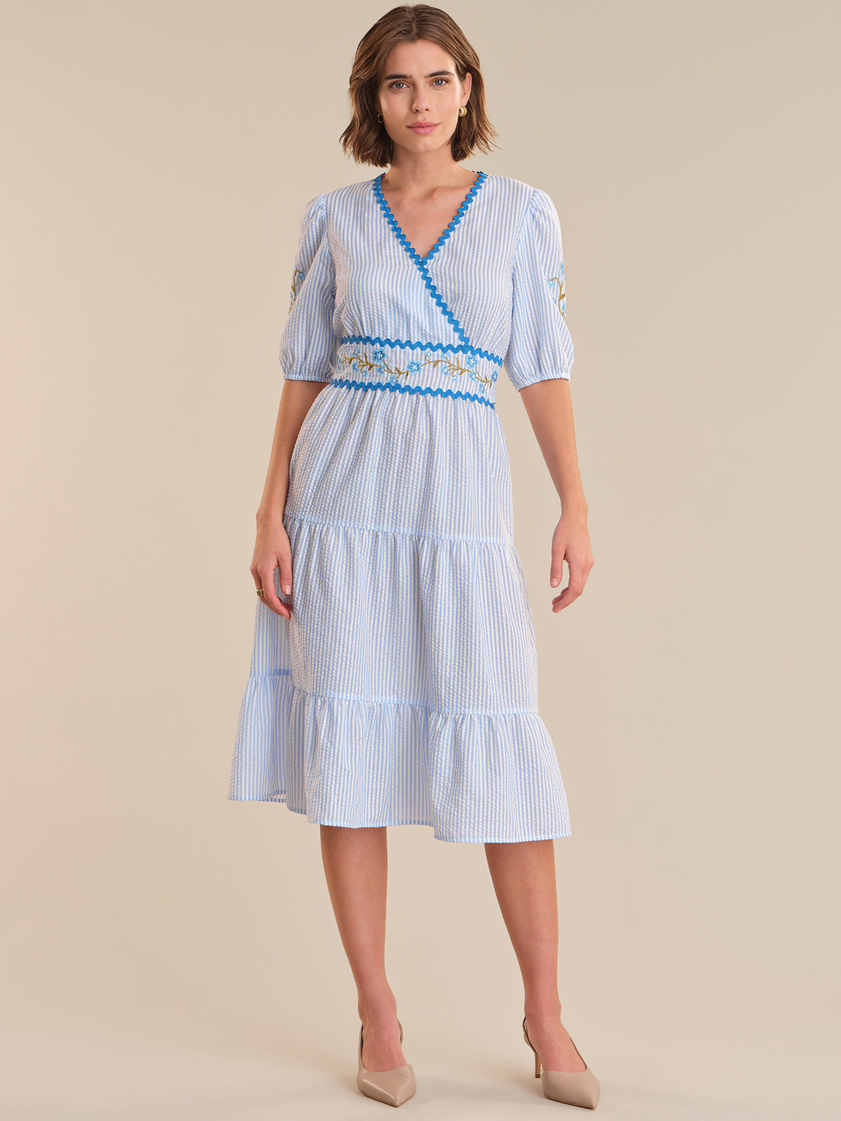 Woman wearing a blue and white striped dress with a belt on a beige background