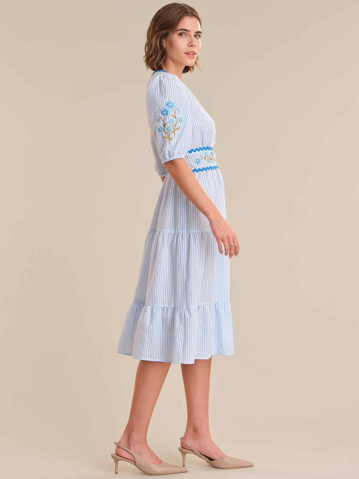 Woman wearing a light blue striped dress with floral embroidery on a beige background