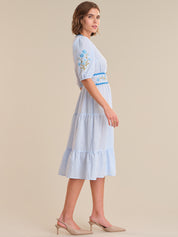 Woman wearing a light blue striped dress with floral embroidery on a beige background