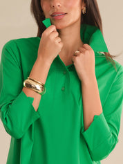 Woman wearing a green shirt with gold jewelry on a neutral background