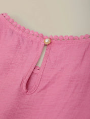 Close-up of a pink garment with decorative trim and a pearl button on a beige background