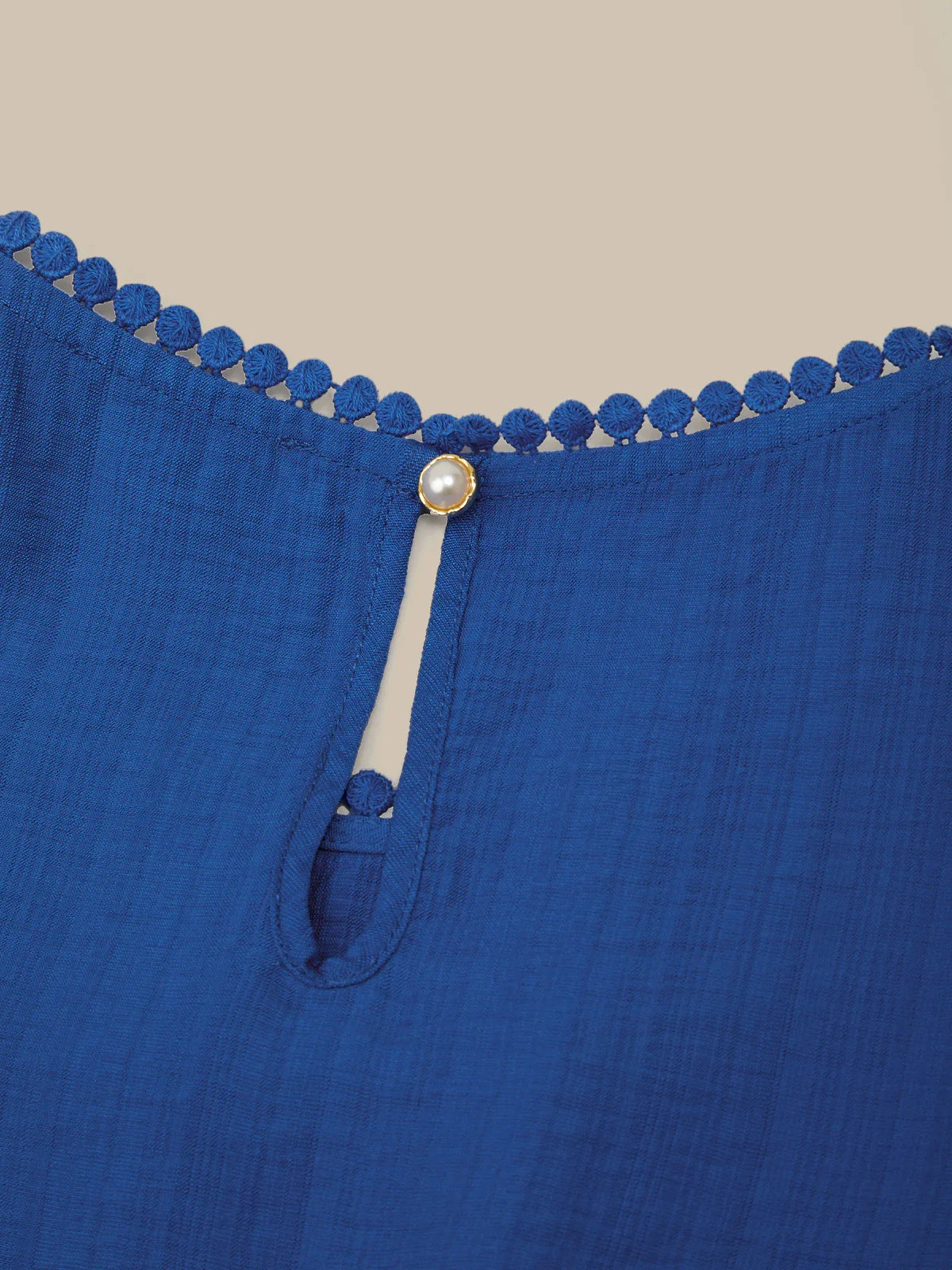 Close-up of a blue garment with decorative trim and button on a beige background