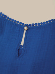 Close-up of a blue garment with decorative trim and button on a beige background