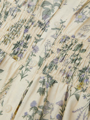Close-up of a floral patterned fabric with green leaves and purple flowers on a beige background.