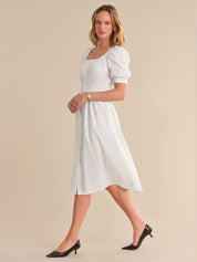 Woman wearing a white dress with puff sleeves against a beige background
