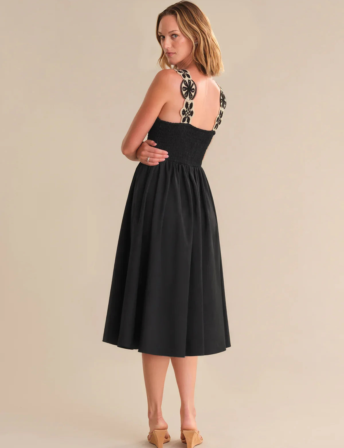 Woman wearing a black dress with floral straps on a beige background