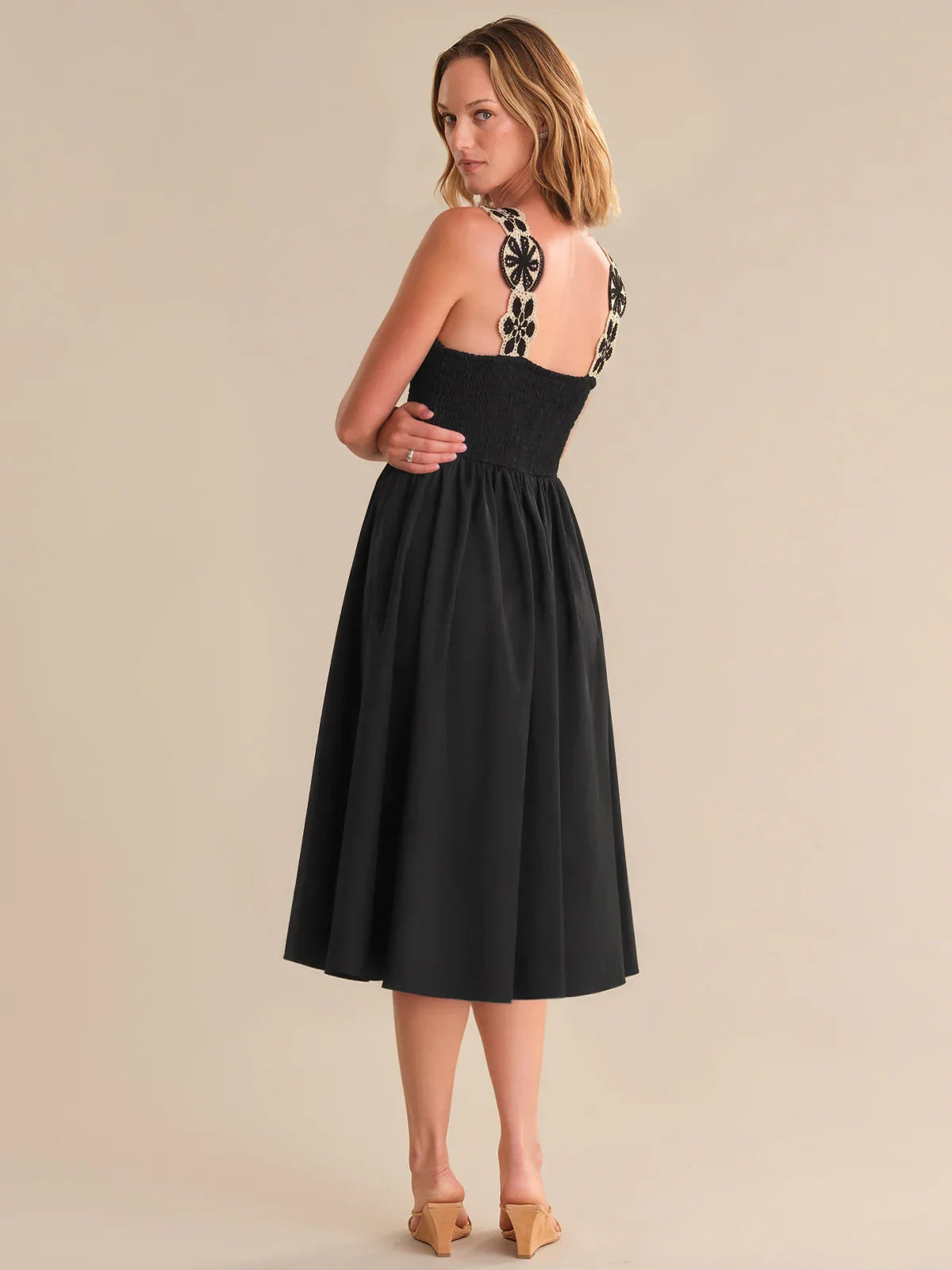 Woman wearing a black dress with floral straps on a beige background