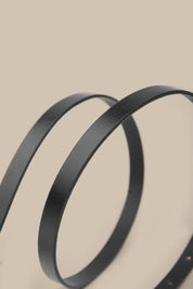 Two black metal belts on a beige background