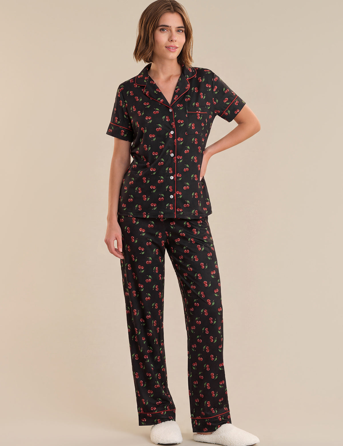 Woman wearing a black pajama set with red floral pattern on a beige background