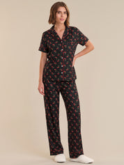 Woman wearing a black pajama set with red floral pattern on a beige background