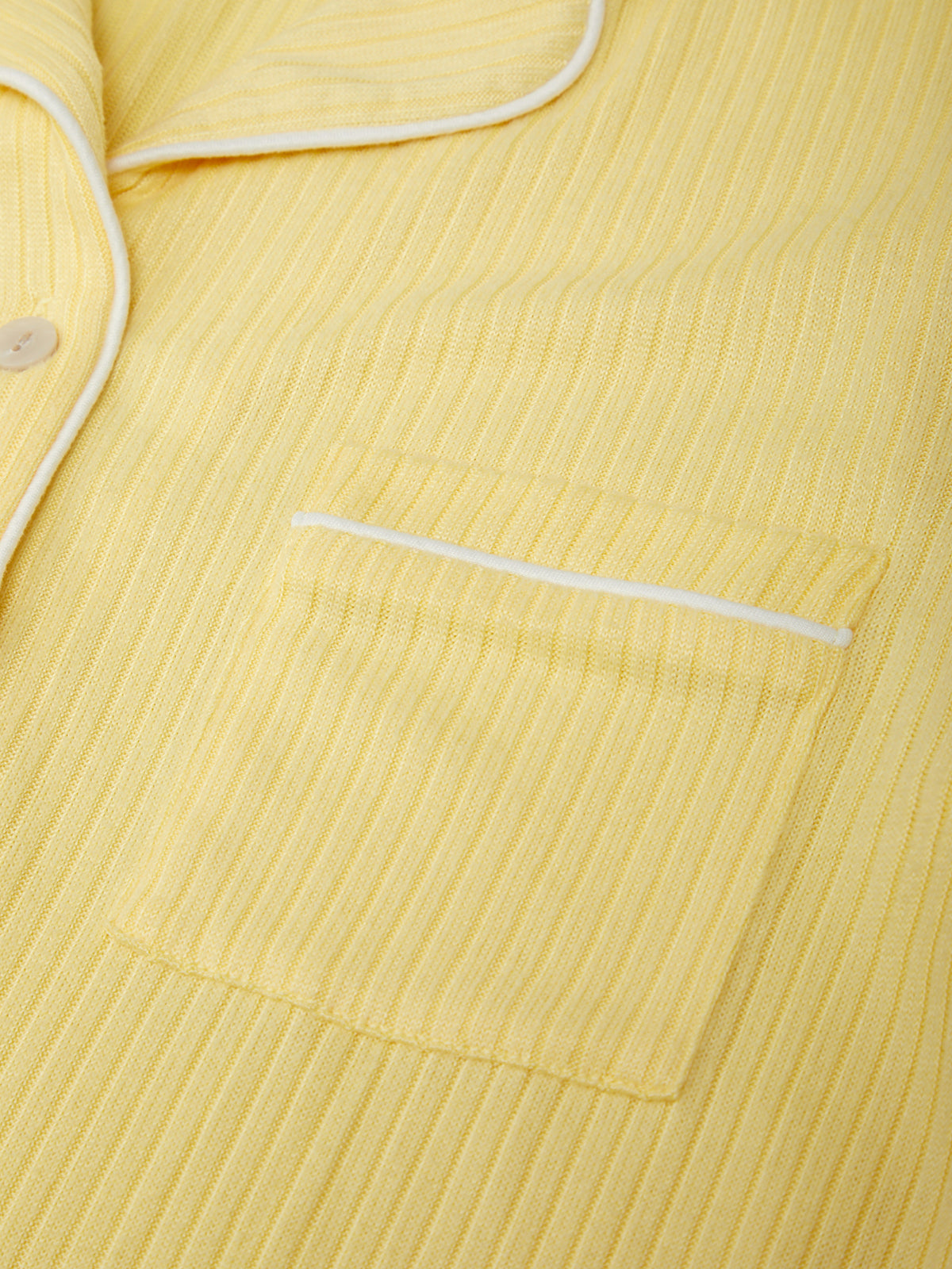 Yellow ribbed fabric with white piping on a close-up of clothing.