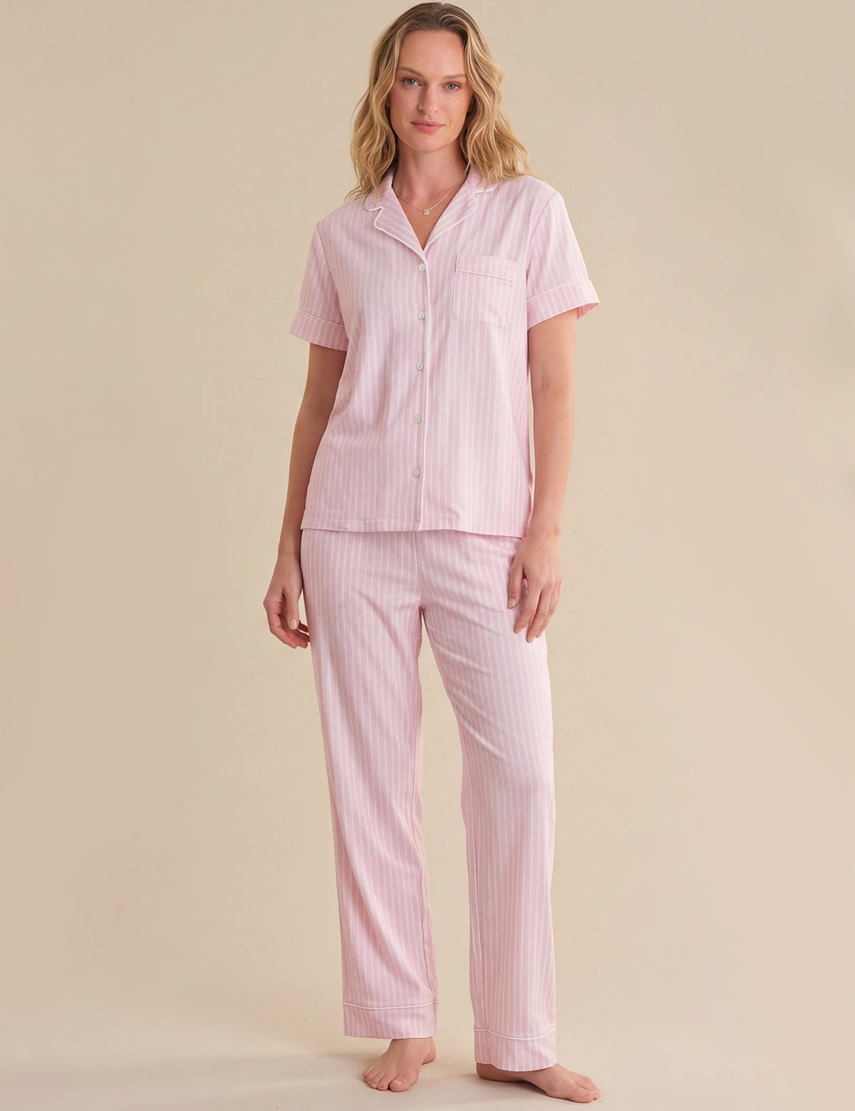 Woman wearing a pink striped pajama set on a beige background