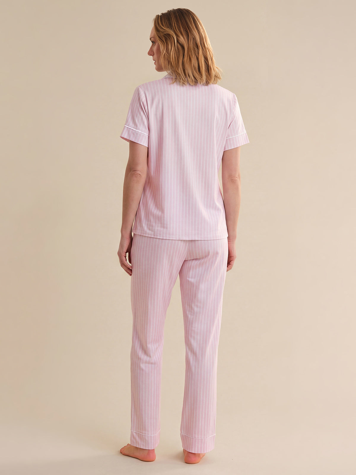 Woman wearing a pink striped pajama set against a beige background