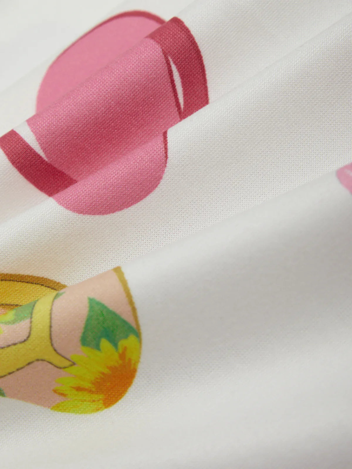 Close-up of fabric with pink heart, yellow shoe, and green leaf design on a white background