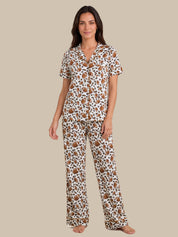 A woman modeling a matching short-sleeve button-front pajama top and wide-leg pajama pants set in a brown and black leopard print on a white background, set against a solid beige studio backdrop.