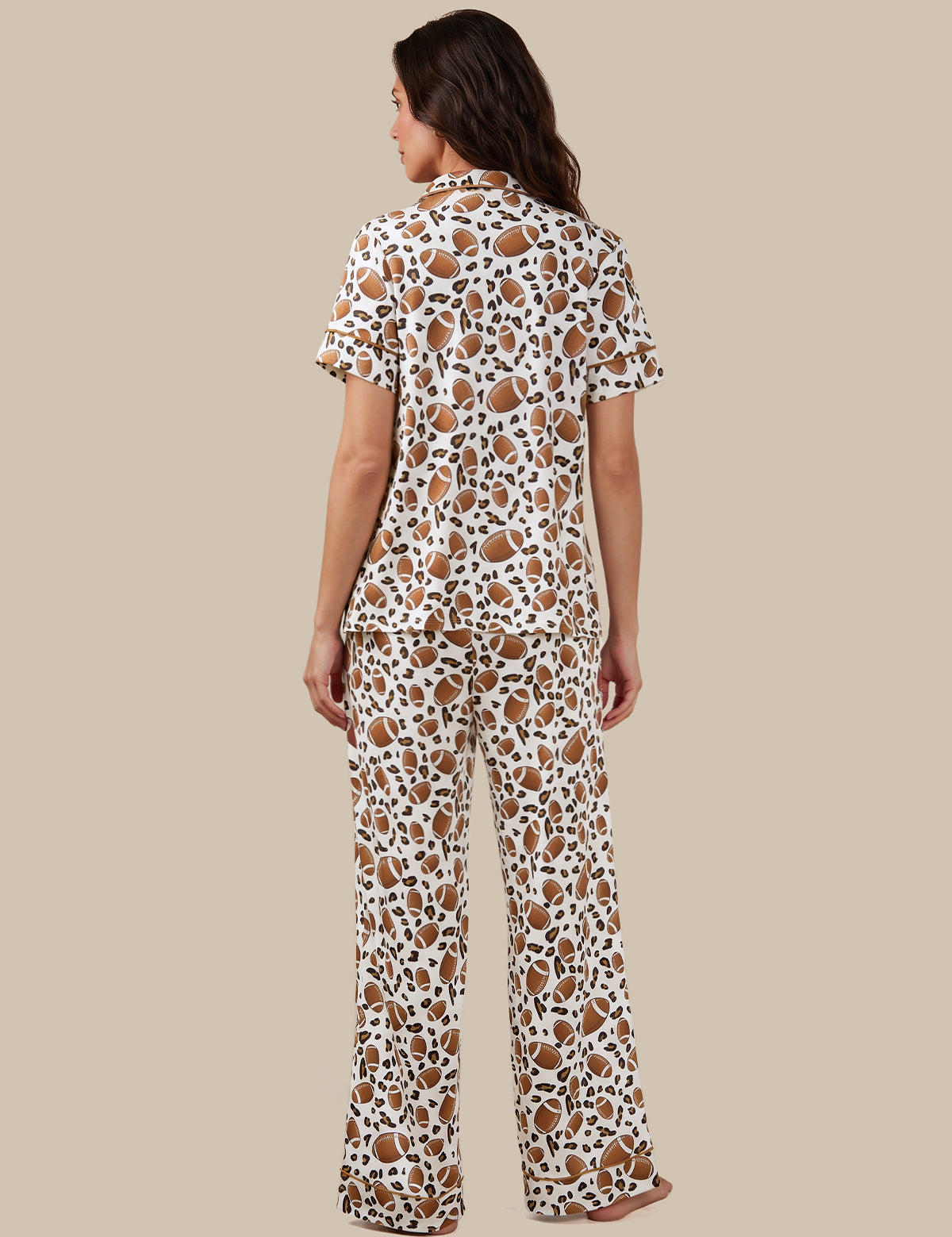 A woman shown from the back wearing a matching short-sleeve button-up pajama shirt and wide-leg pants set in a brown and black spotted animal print on a white base, set against a solid beige background.
