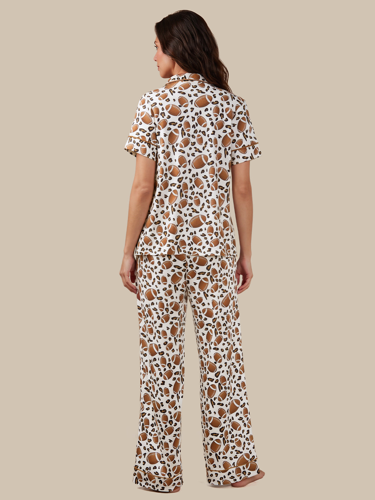A woman shown from the back wearing a matching short-sleeve button-up pajama shirt and wide-leg pants set in a brown and black spotted animal print on a white base, set against a solid beige background.