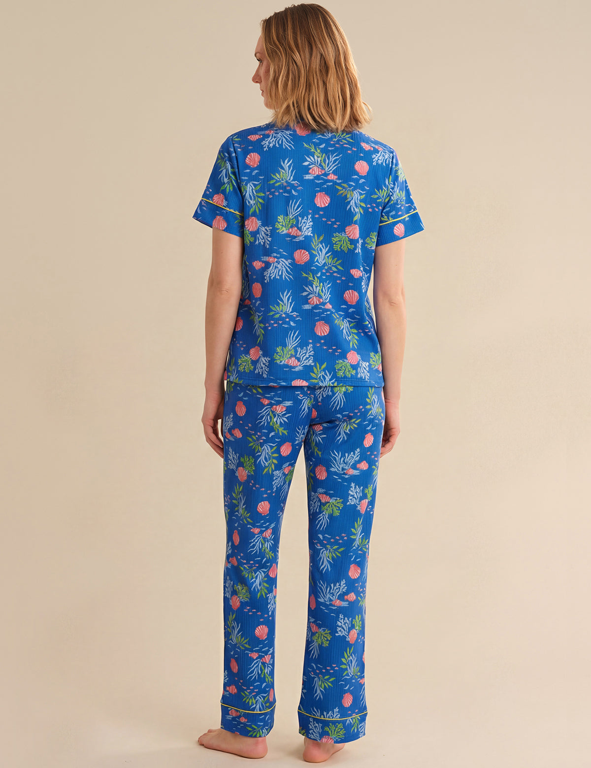 Person wearing a blue tropical sea pajama set on a beige background