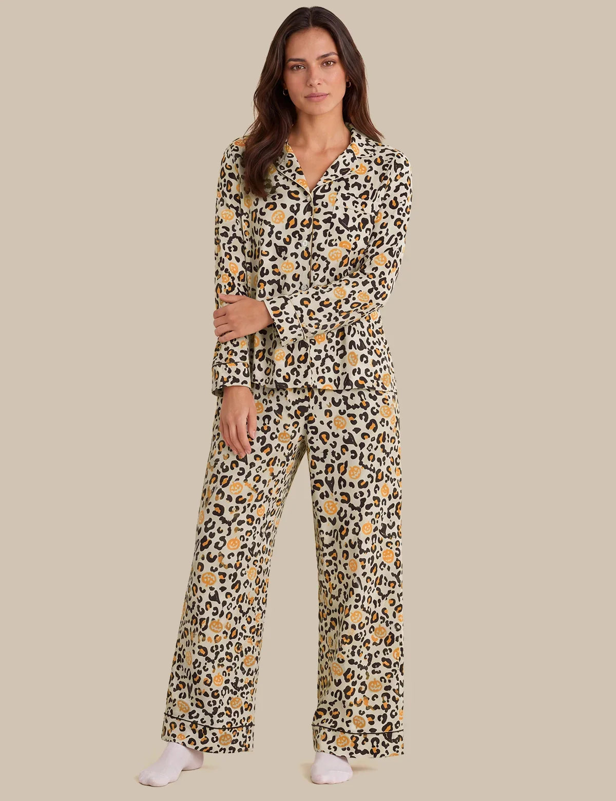 A woman modeling a long-sleeve matching pajama set with a beige, black, and brown leopard print pattern, featuring a collared shirt top and wide-leg pants, set against a solid beige background.