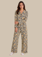 A woman modeling a long-sleeve matching pajama set with a beige, black, and brown leopard print pattern, featuring a collared shirt top and wide-leg pants, set against a solid beige background.
