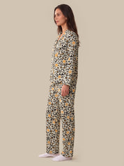 A woman modeling a matching two-piece pajama set with a leopard print pattern and small yellow floral accents, shown in profile against a solid beige background.