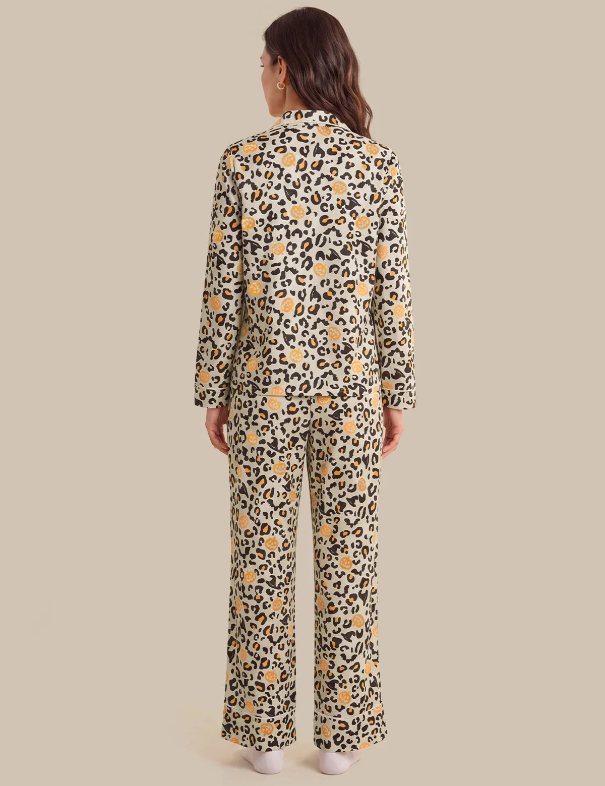 A woman viewed from the back wearing a matching long-sleeve button-front top and wide-leg pants set in a beige animal print with black spots and yellow floral accents, against a solid beige studio background.