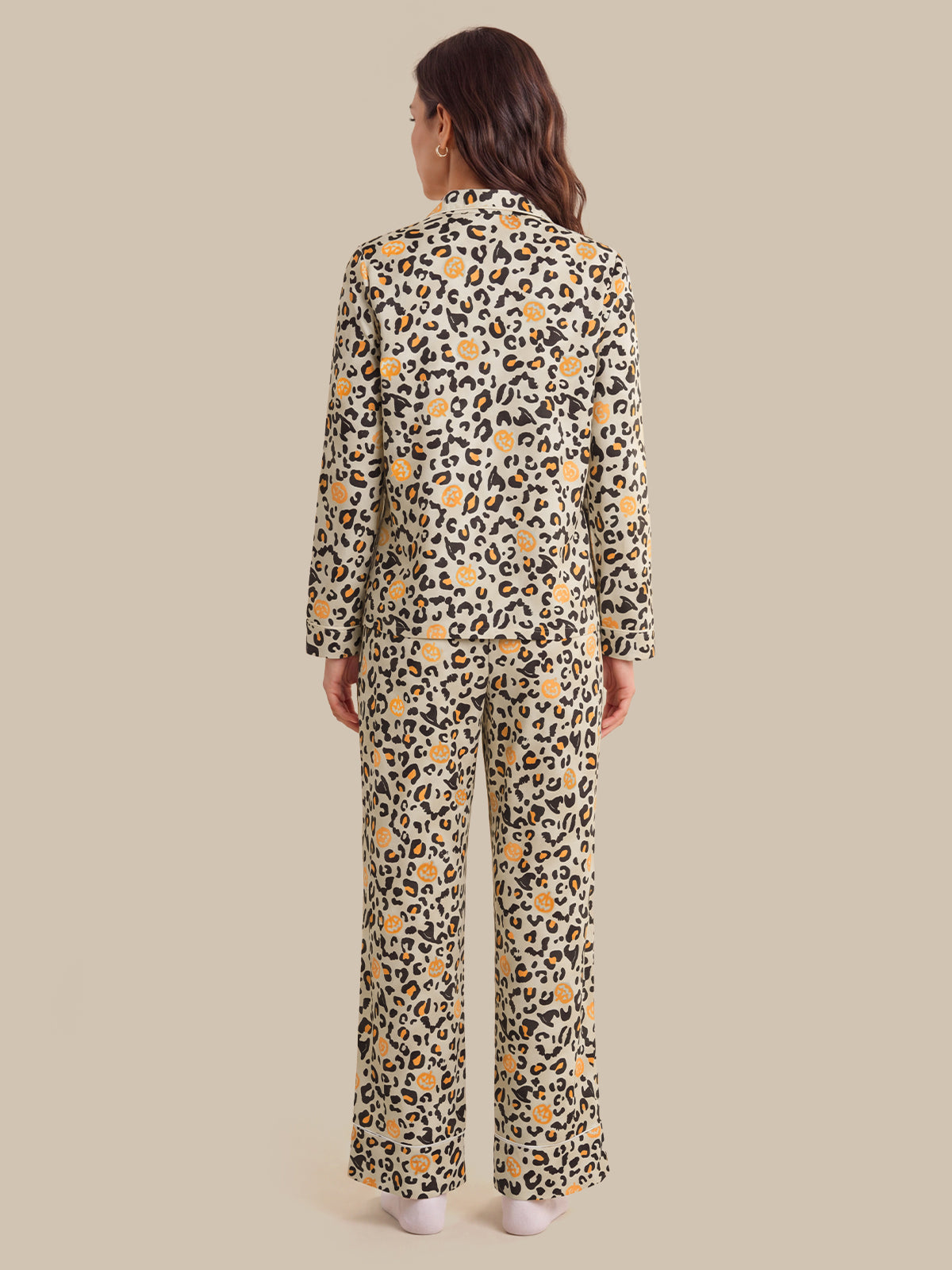 A woman viewed from the back wearing a matching long-sleeve button-front top and wide-leg pants set in a beige animal print with black spots and yellow floral accents, against a solid beige studio background.