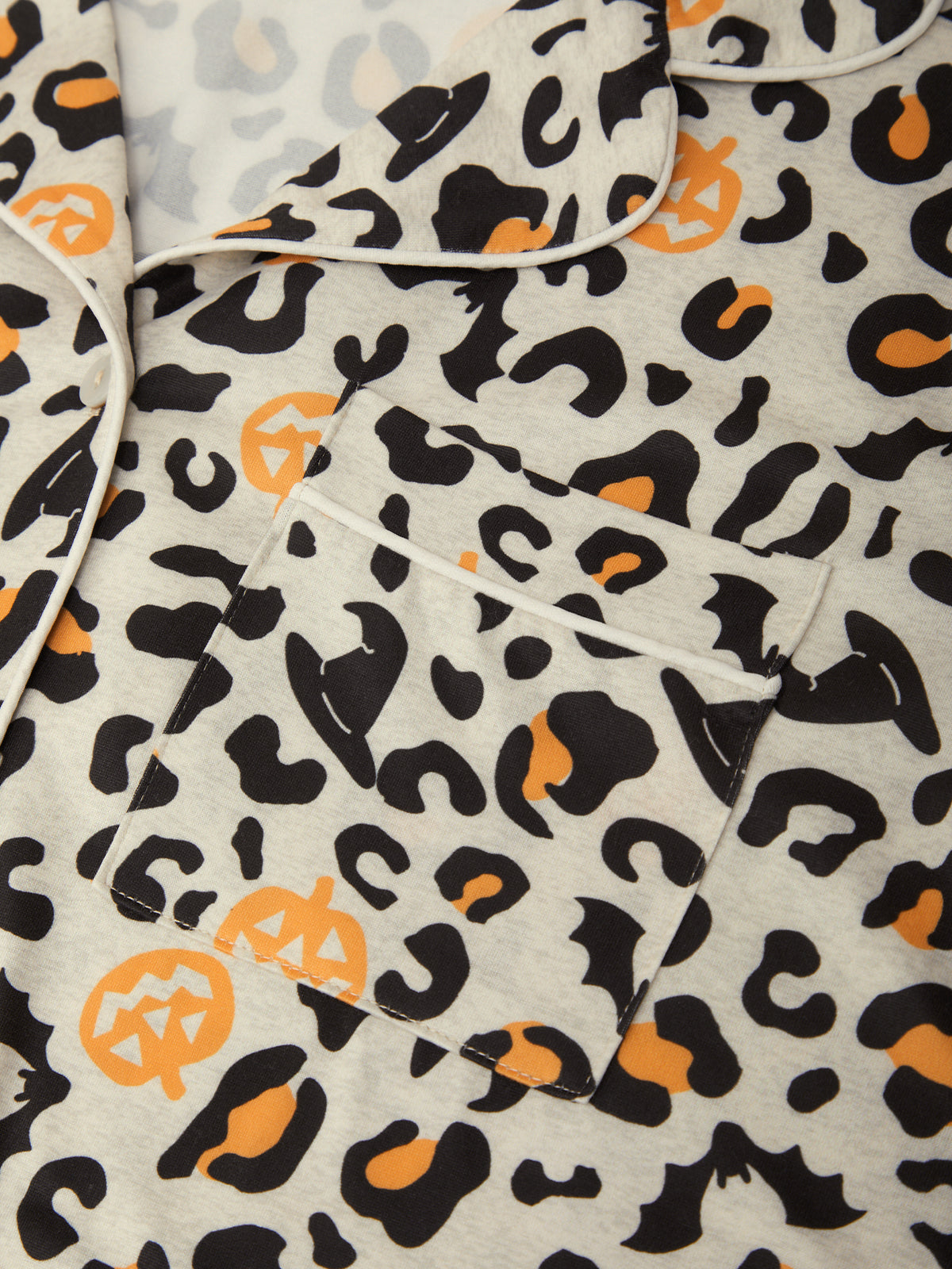 Close-up of a pajama top with a Halloween-themed animal print featuring black and orange pumpkin and bat motifs on a light gray background.