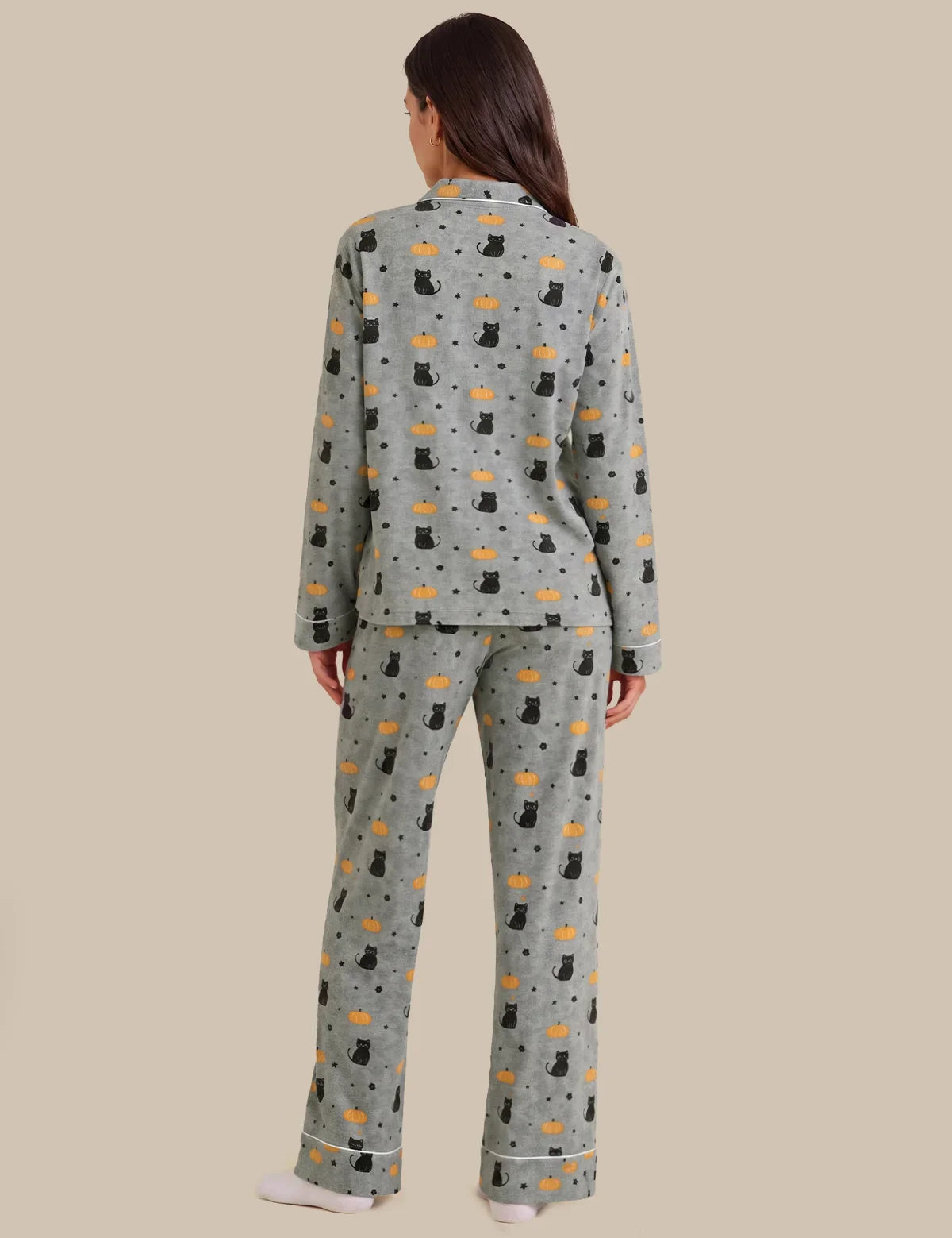 A woman viewed from the back wearing a matching pajama set with a light gray base and an allover print of black cats, orange fish, and small black dots, against a solid beige background.