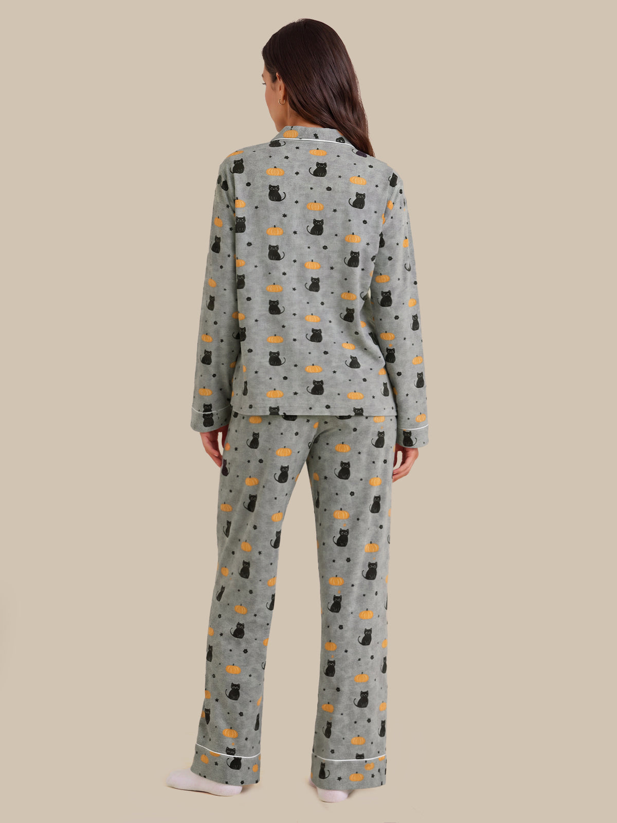 A woman viewed from the back wearing a matching pajama set with a light gray base and an allover print of black cats, orange fish, and small black dots, against a solid beige background.