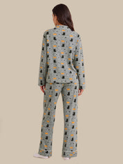 A woman viewed from the back wearing a matching pajama set with a light gray base and an allover print of black cats, orange fish, and small black dots, against a solid beige background.