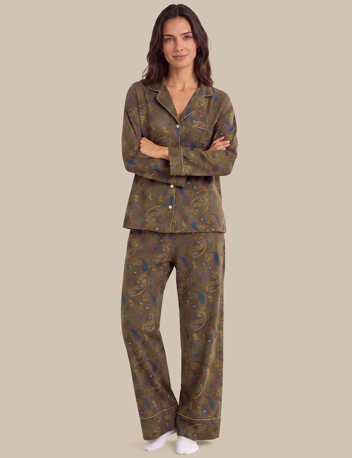 A woman modeling a two-piece pajama set with a brown paisley pattern, featuring a long-sleeve button-up top and matching pants, against a solid beige background.