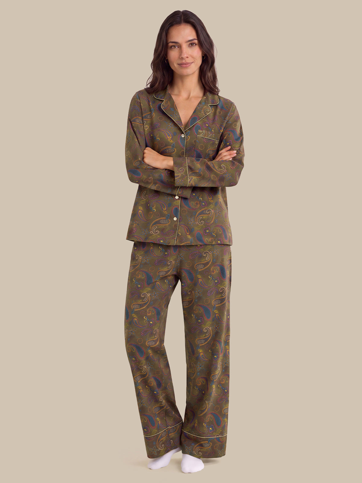 A woman modeling a two-piece pajama set with a brown paisley pattern, featuring a long-sleeve button-up top and matching pants, against a solid beige background.